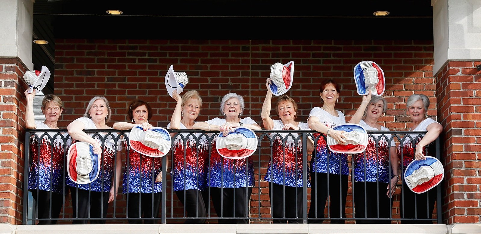 Sweet Harmony singers waving cowboy hats from a balcony