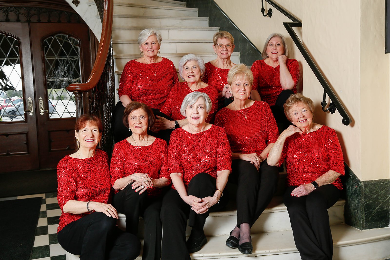 Sweet Harmony singers in red on a grand staircase